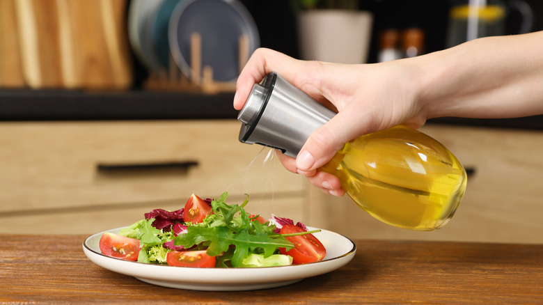 A person spraying olive oil onto a salad