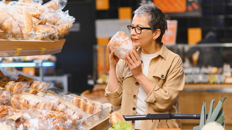 Woman smelling loaf of bread in grocery store bakery