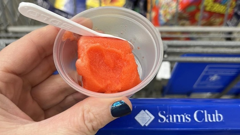 woman holds sample cup next to Sam's Club cart