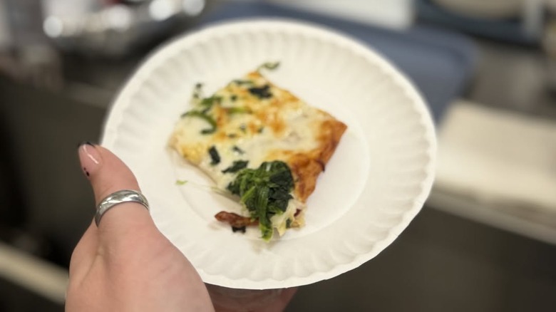 person holding a sample of pizza on a paper plate