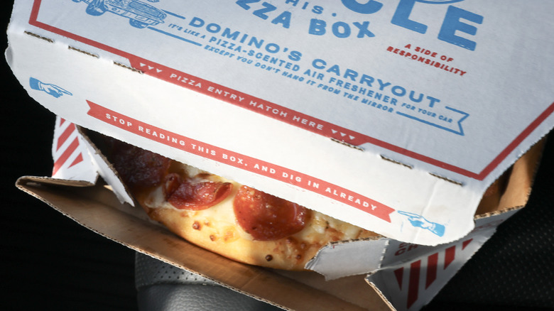 A photo of the edge of an open Domino's Pizza box showing a peek of a pepperoni pizza from under the lid.