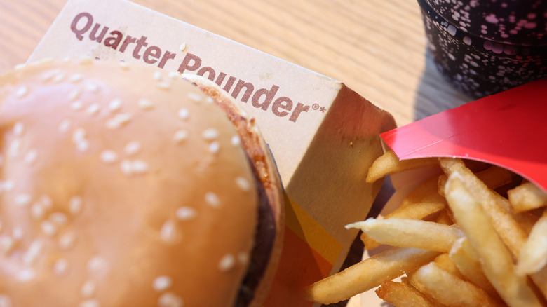 A top view of half a McDonald's Quarter Pounder on top of its disposable carton and some fries on the side