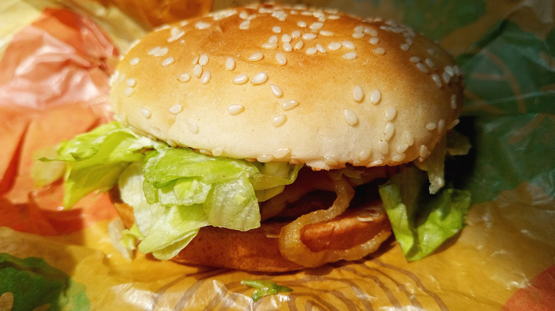 A close-up of an unwrapped Burger King wrapper showing the sesame buns, lettuce, patty, and onions