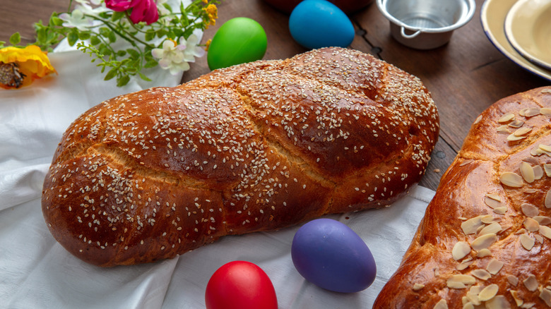 Easter breads baked with sesame seeds or sliced almonds surrounded by painted eggs and flowers