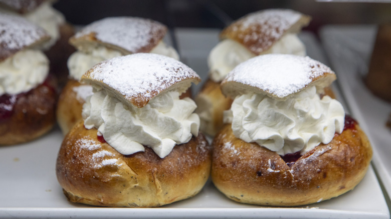 Semla buns on square plate, topped with whipped cream and powdered sugar