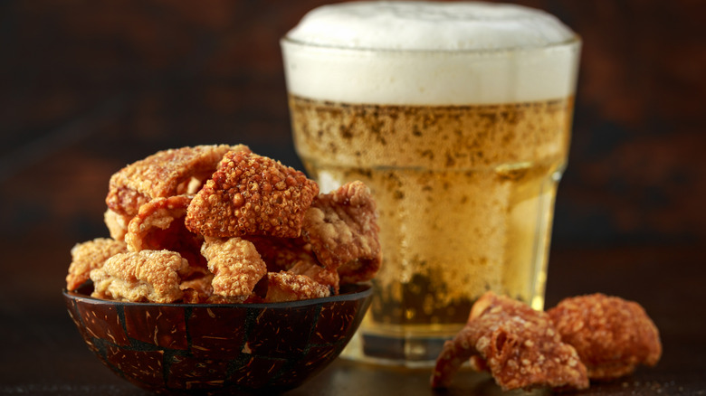 A bowl overflowing with pork scratchings with a beer in the background