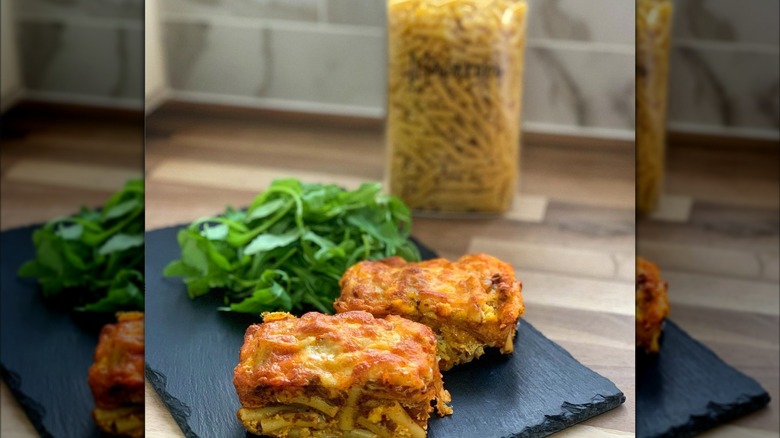 mini baked macaroni loafs on a black slate plate with greens