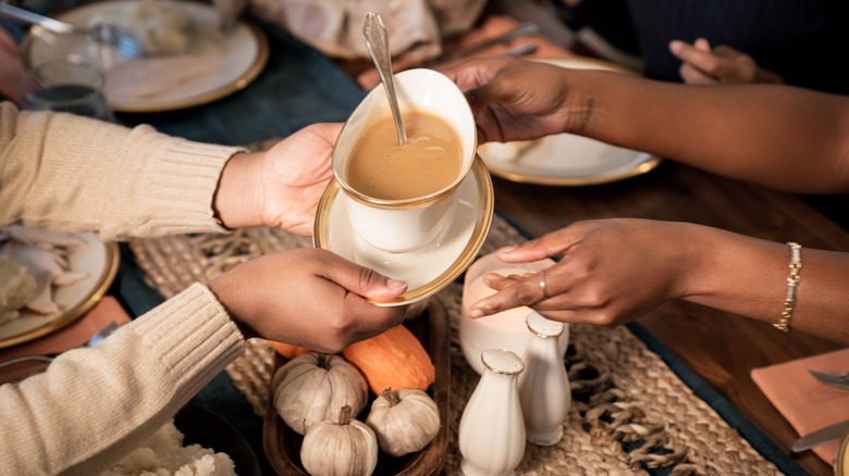 hands passing gravy boat at table