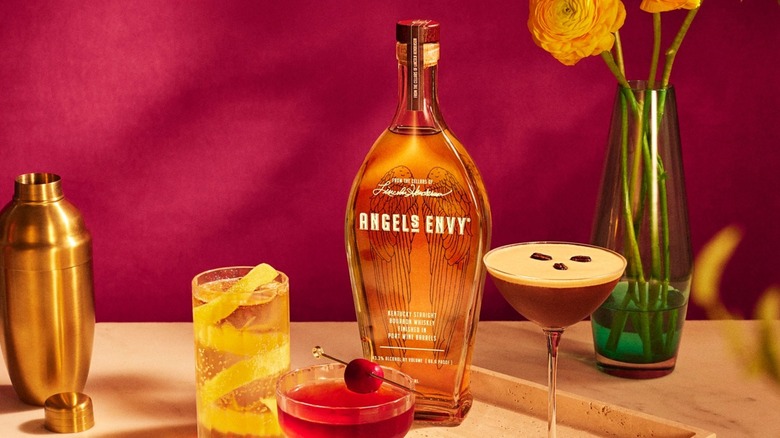 Bottle of Angel's Envy on table with cocktails, shaker, and flowers