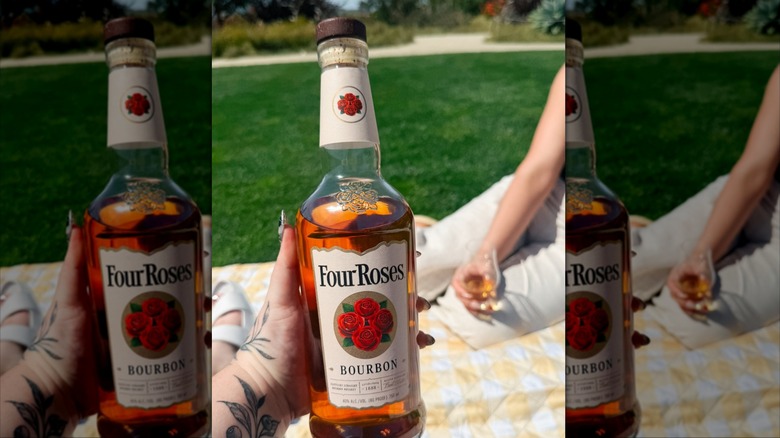 Hand holding Four Roses bottle with person holding glass blurred in background on picnic blanket
