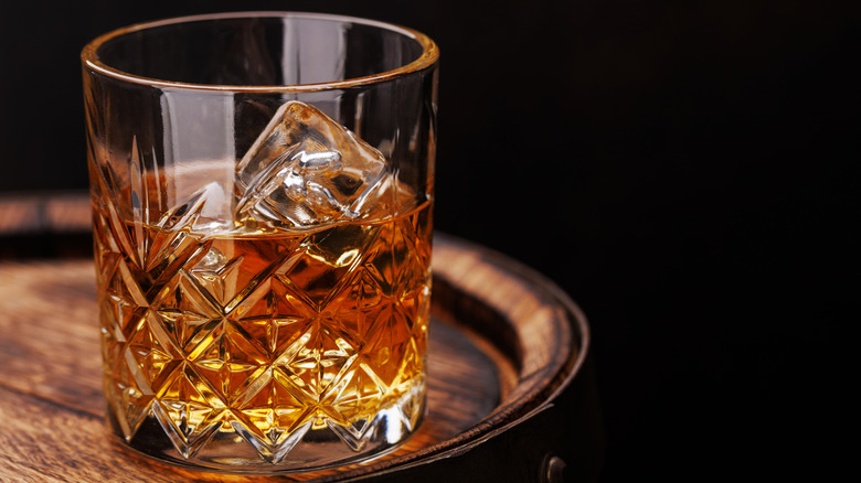 Glass of bourbon and ice on barrel