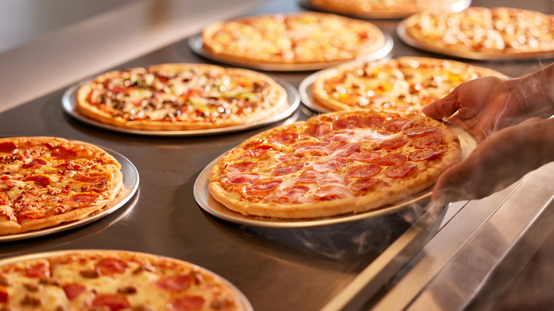 Hands setting a hot pepperoni pizza onto the pizza buffet bar at Peter Piper Pizza