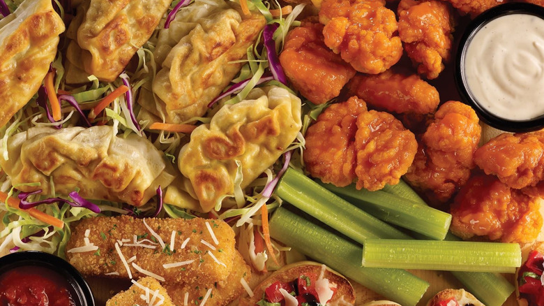 A close-up of a plate of mixed appetizers from TGI Fridays featuring Buffalo chicken, mozzarella sticks, potstickers
