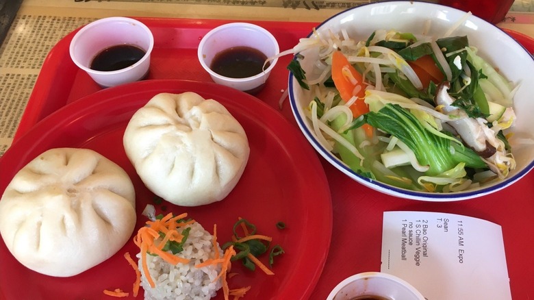 Pork Bao from Zoe Ma Ma restaurant on plate next to side salad and dipping cups of sauce on tray