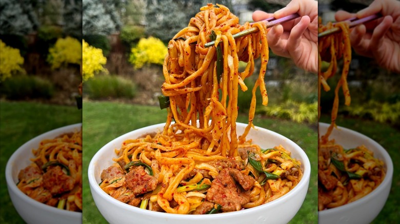 Chopsticks lifting hand-pulled noodles from a bowl with sauce and pieces of meat