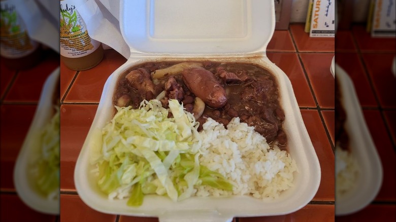 Styrofoam to go container from Jamaica Kitchen restaurant with shredded lettuce, white rice, and stewed peas with pig tails