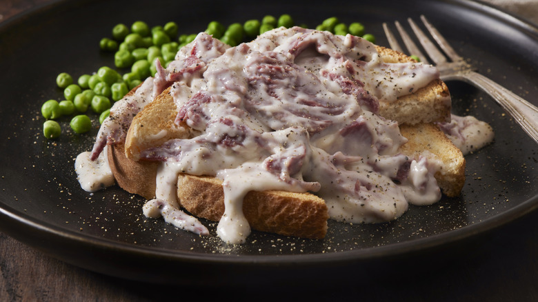 peppered chipped beef gravy over toast with green peas on black plate