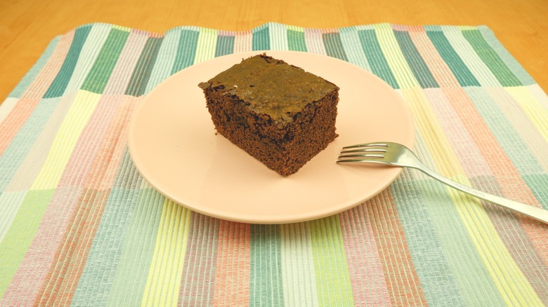 chocolate wacky cake on a white plate on a striped placemat and a fork