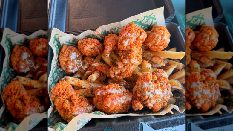 Buffalo chicken wings atop a pile of french fries, all in a black takeout container