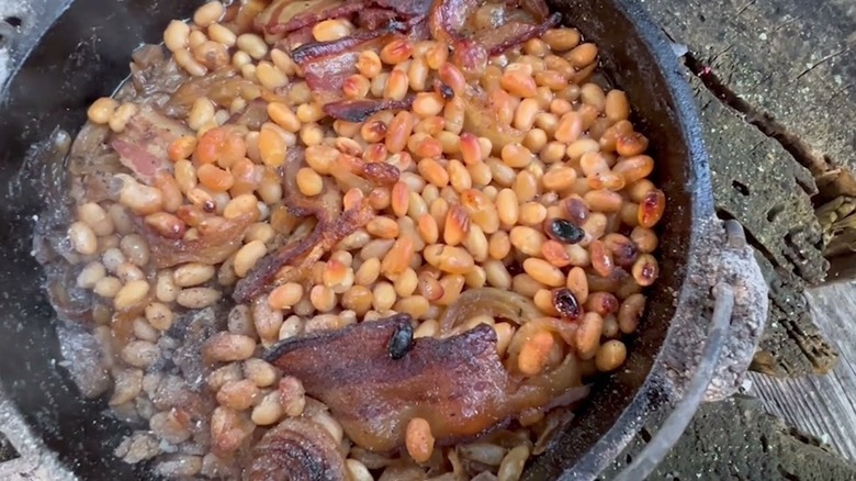 A cast iron pot of beans on a rustic wood surface outdoors