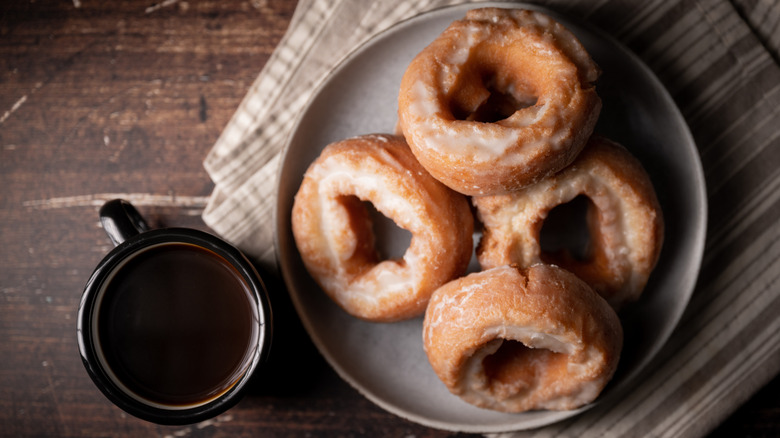 A plate of old-fashioned donuts on a wood table next to a cup of coffee