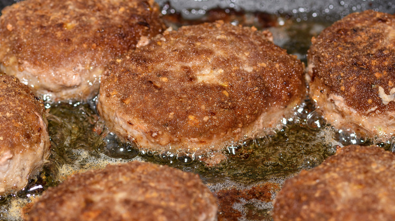 Ground meat patties frying on a cooktop