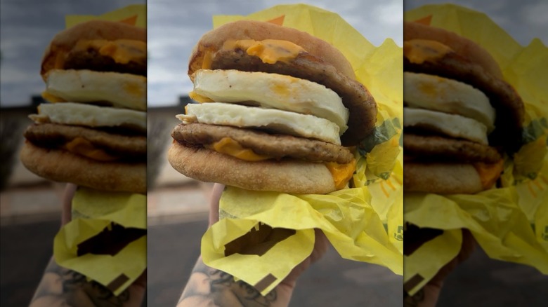 Hand holding a McDonald's egg Mcmuffin that has two eggs and two sausage patties inside