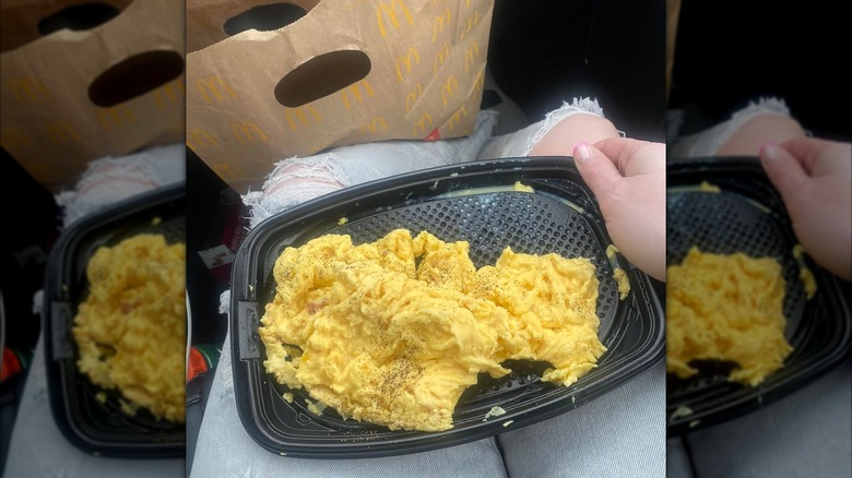 Person sitting with plastic tray of McDonald's scrambled eggs in lap