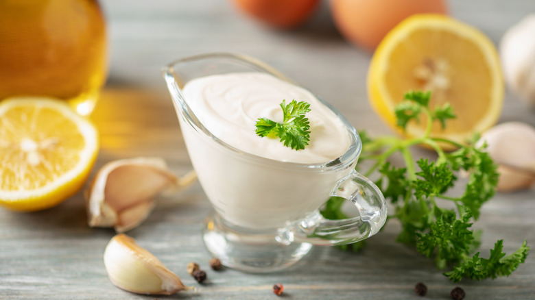 A glass serving jug filled with aioli and topped with a sprig of fresh parsley