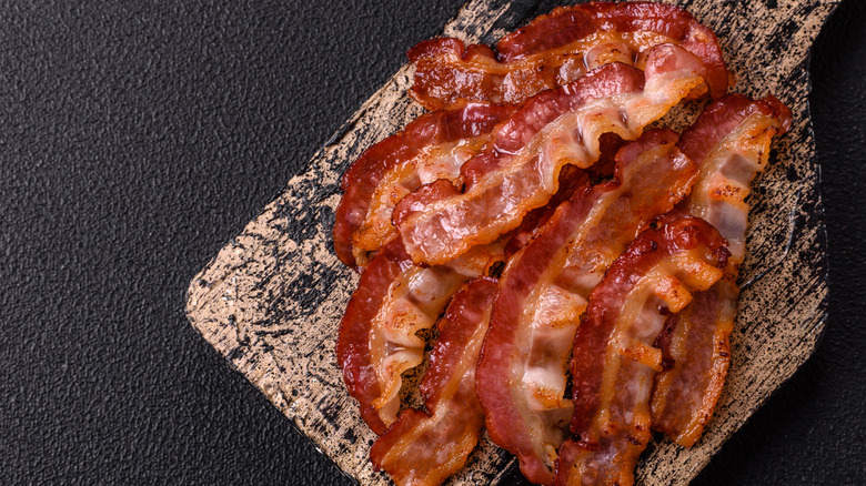 Cooked bacon strips sitting on a wooden cutting board