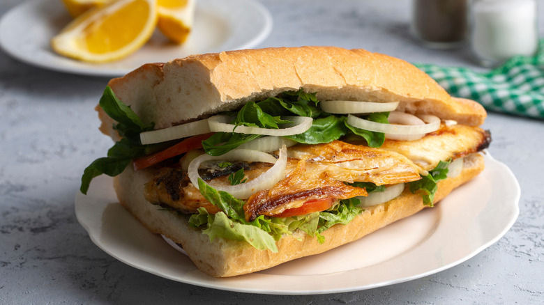 Fish sandwich topped with onions, greens, and tomato