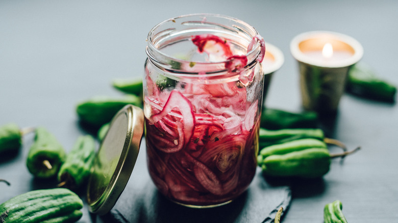 A glass jar filled with pickled red onions surrounded by green peppers
