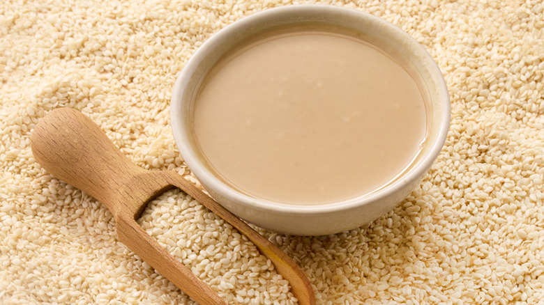 White bowl of tahini surrounded by sesame seeds