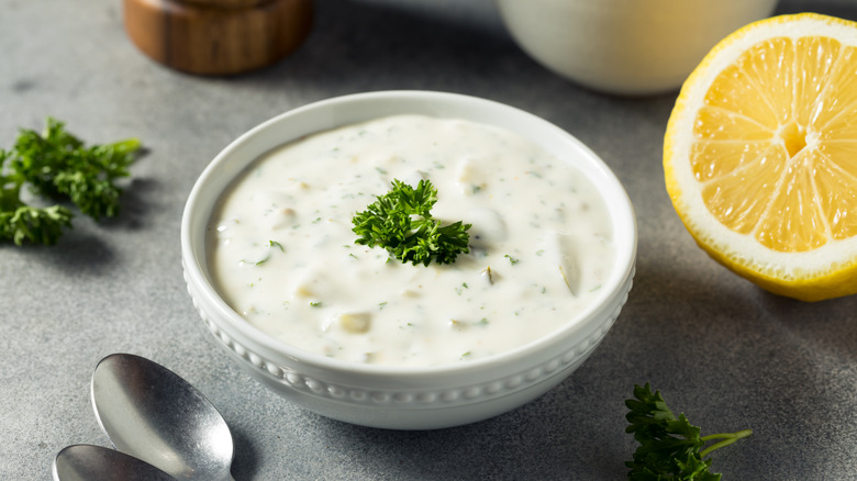 White bowl of tartar sauce topped with fresh parsley next to half a lemon