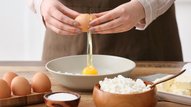 hands cracing an egg into a bowl with some cottage cheese