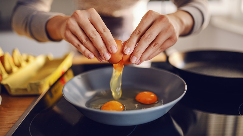 hands cracking eggs into a frying pan