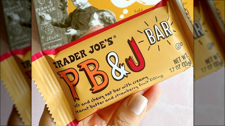 Hand holds a wrapped Trader Joe's PB&J Bar over the product box