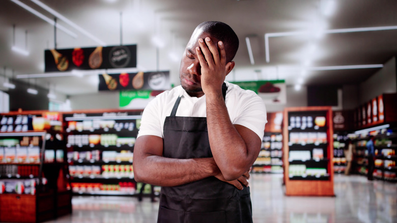 A grocery store employee resting his head on his hand
