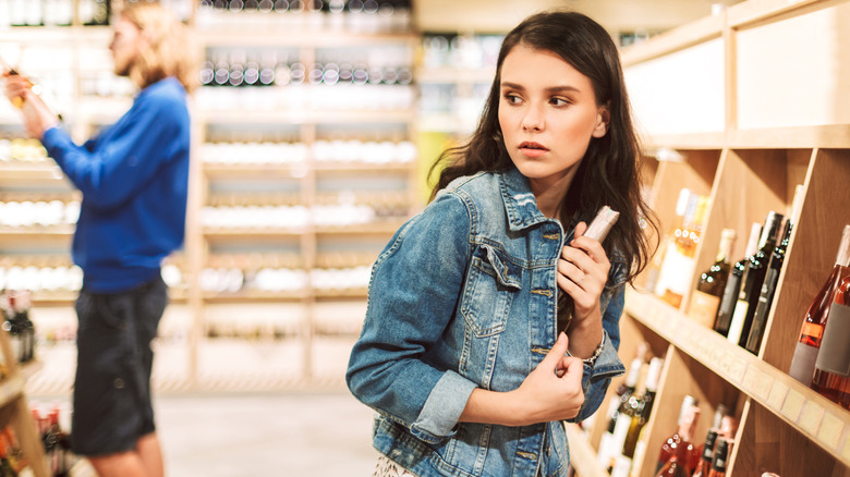 A woman stealing wine by putting a bottle in her jacket