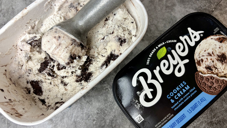 A carton of Breyers Cookies & Cream ice cream unopened with ice cream scoop inside ice cream