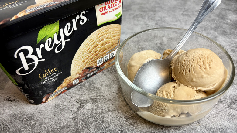 A carton of Breyers Coffee ice cream next to a clear bowl with scoops of the ice cream and a spoon