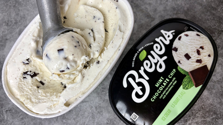 A carton of Breyers Mint Chocolate Chip ice cream opened with an ice cream scoop inside the tub of ice cream