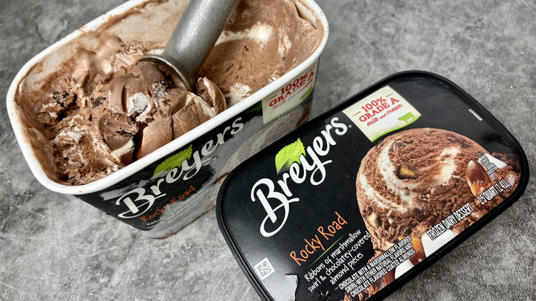 A carton of Breyers Rocky Road ice cream opened with ice cream scoop dipping into the ice cream