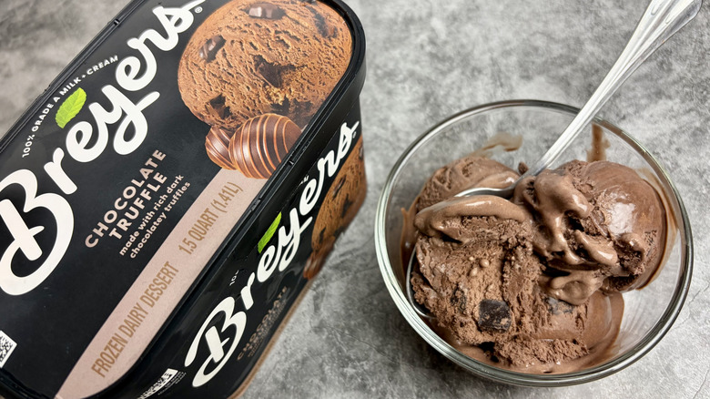 A carton of Breyers Chocolate Truffle ice cream next to a clear bowl with scoops of the ice cream and a spoon