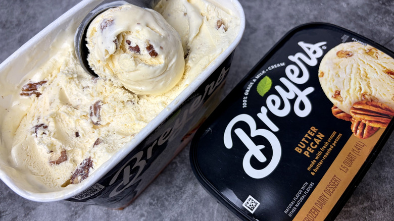 A carton of Breyers Butter Pecan ice cream opened with an ice cream scoop dipping into the ice cream