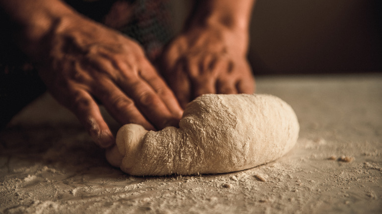 A close-up of hands kneading bread dough on a floured surface