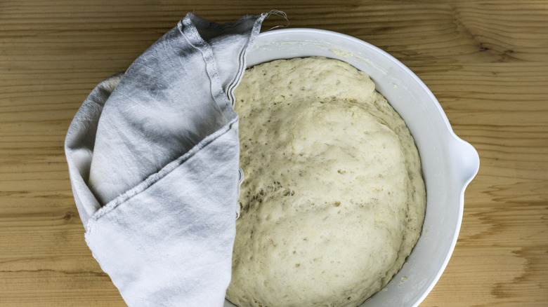 Overhead view of dough in a mixing bowl half-covered with a dish cloth