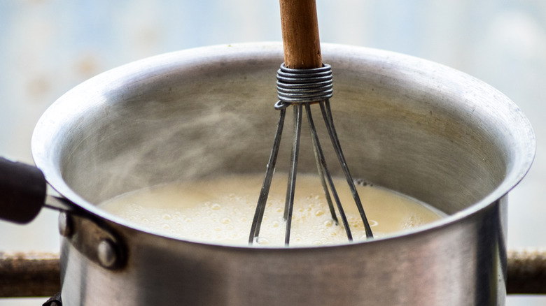 Milk being heated in a saucepan with a metal whisk in it