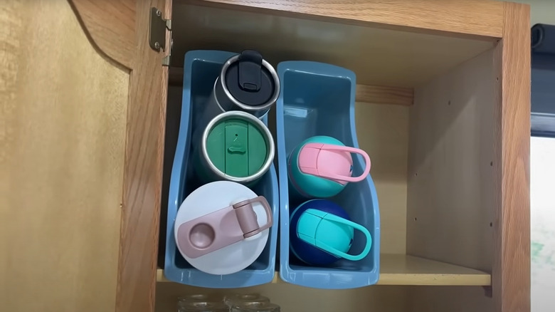 Two blue dollar tree book bins used as an organizer in a cabinet for water bottles and tumblers