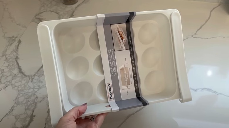 a hand holding up an egg holder shelf from the Dollar Tree with a marble counter on the background.